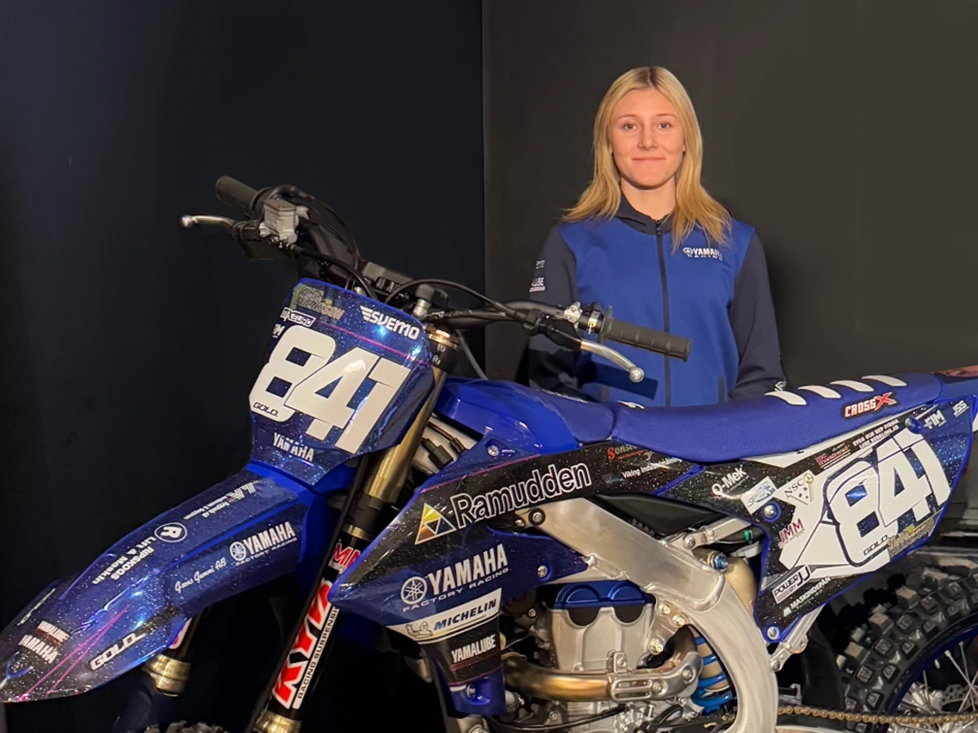 Tjej står vid blå motocross med en Ramudden-logo